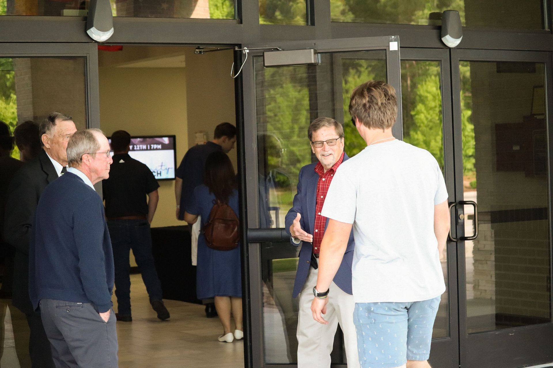 A group of people are standing in front of a glass door talking to each other.