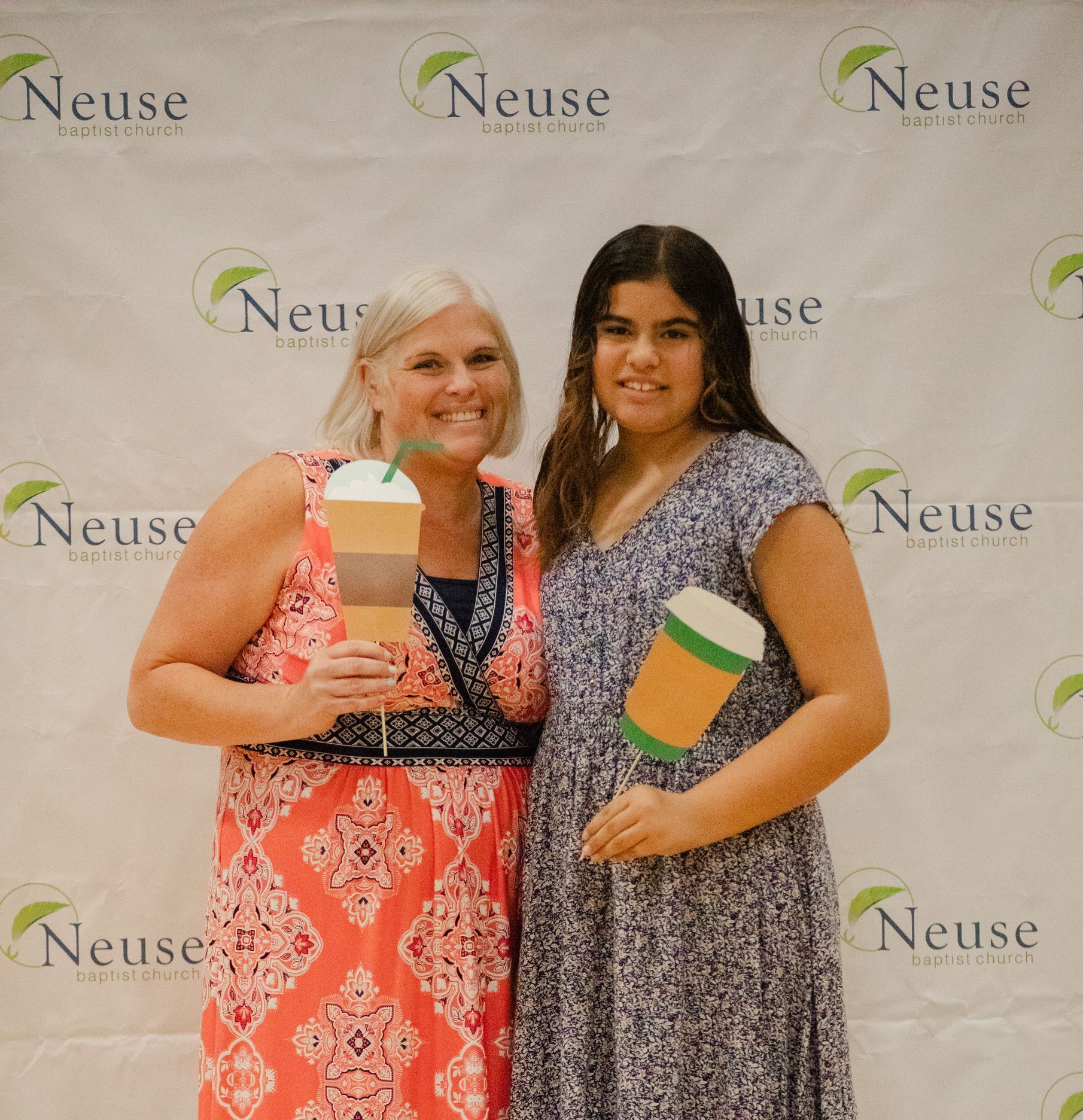 Woman and girl pose in front of a backdrop, holding paper coffee cutouts.