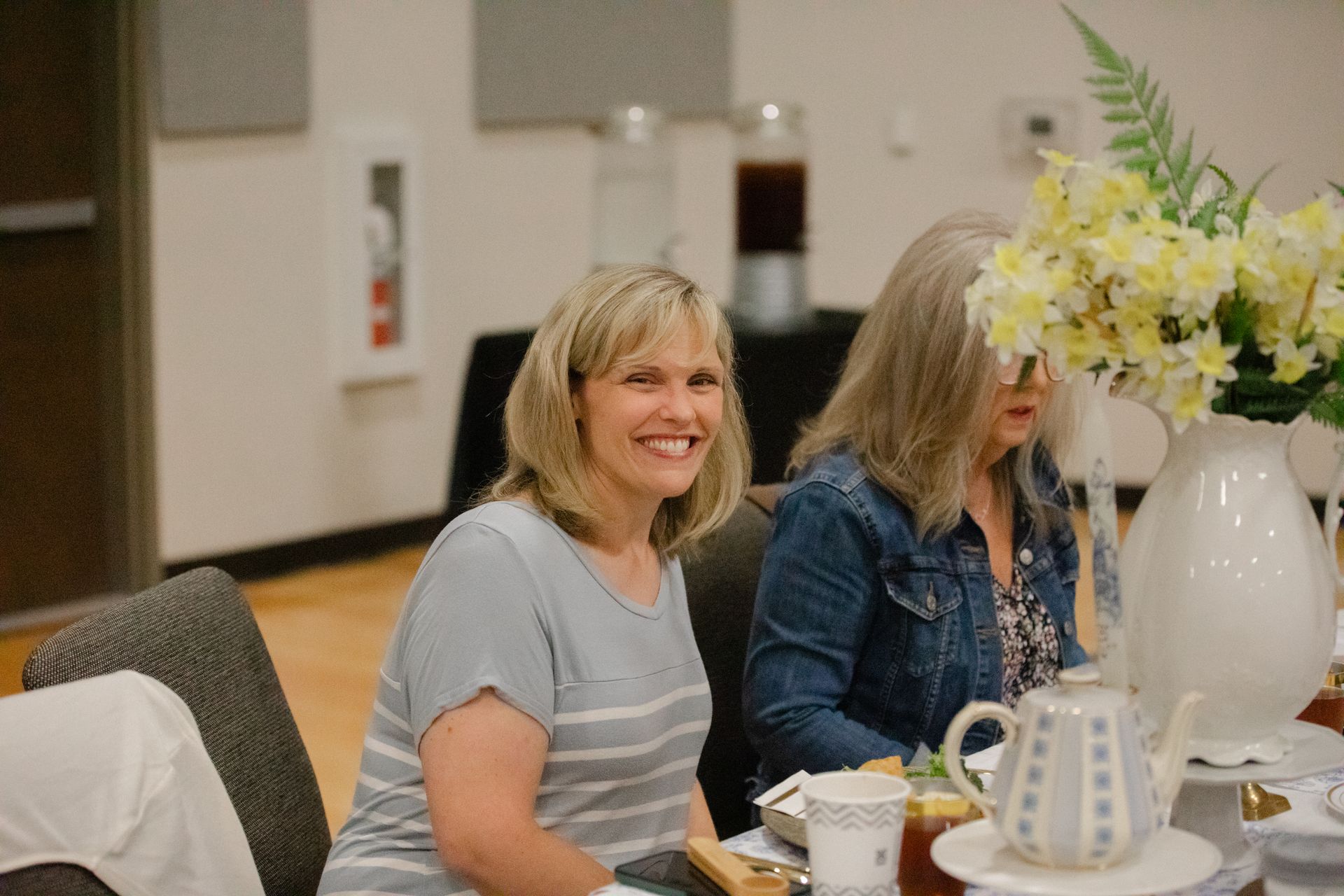 Two women are sitting at a table with a vase of flowers.