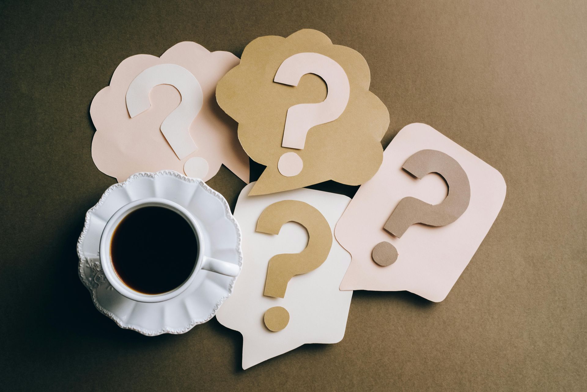 Paper cut-out question marks in beige, white, and pink speech bubbles on a dark green background.