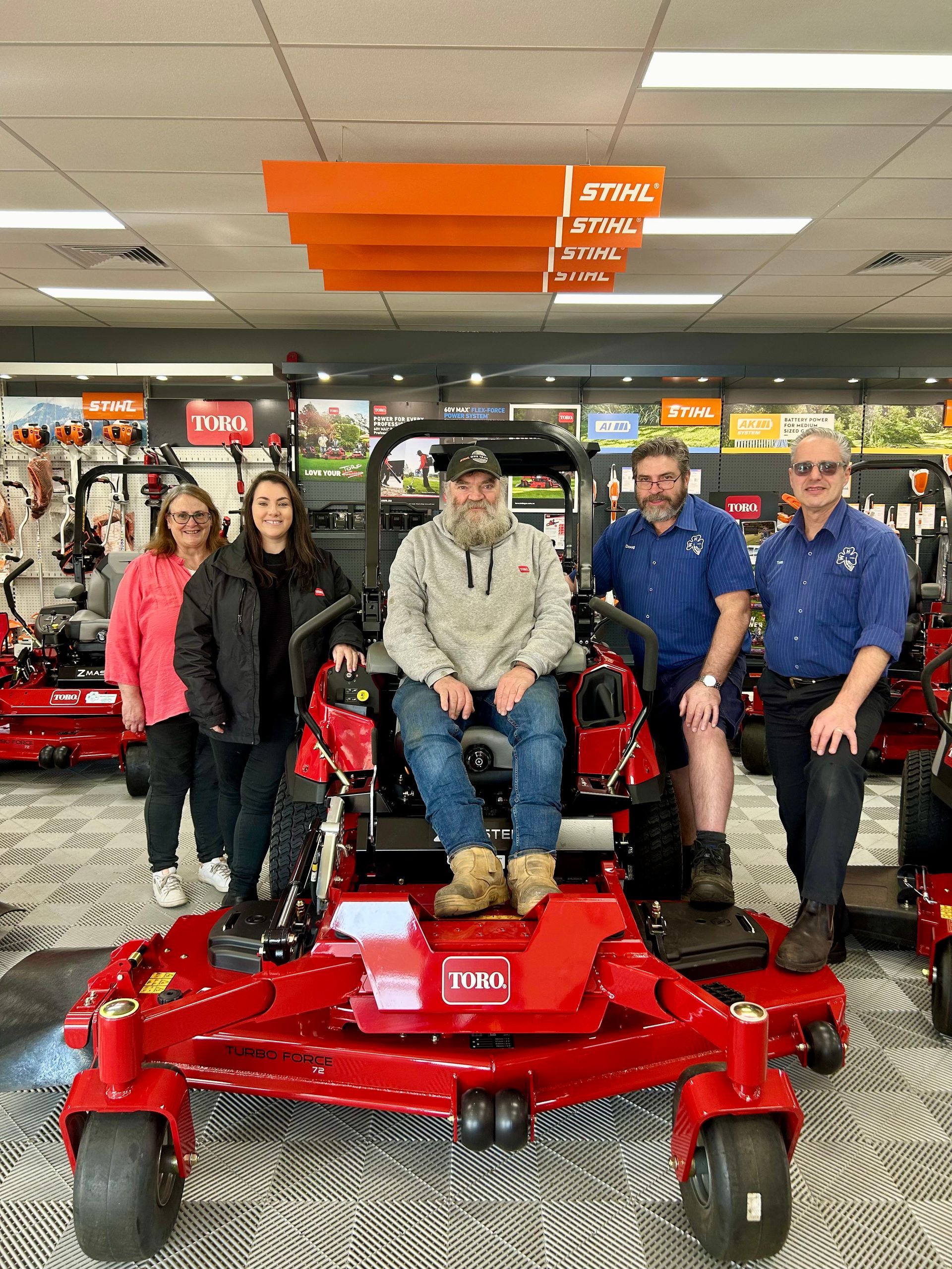 A Group of People Are Standing Around a Red Lawn Mower in a Store — Ireland's Machinery Pty Ltd In Braemar, NSW