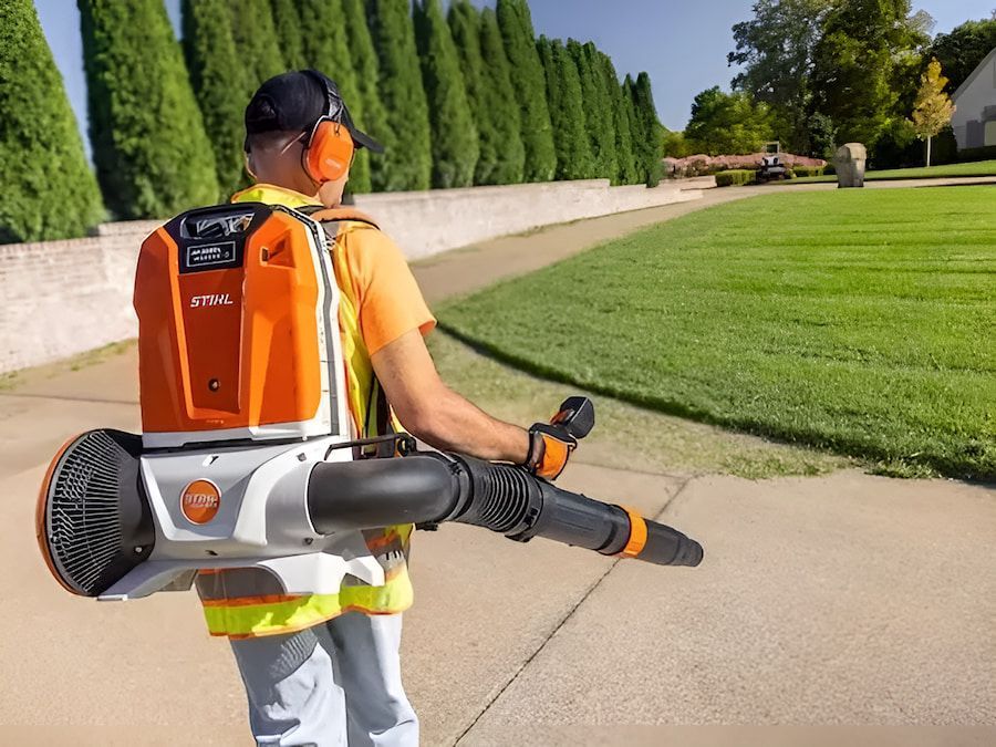 A Man is Walking Down a Sidewalk With a Backpack Blower — Ireland's Machinery Pty Ltd in Braemar, NSW