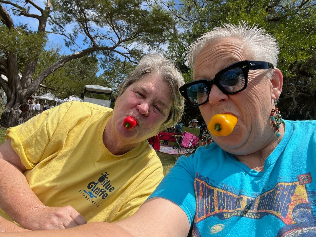 Two women are sitting next to each other with tomatoes in their mouths.