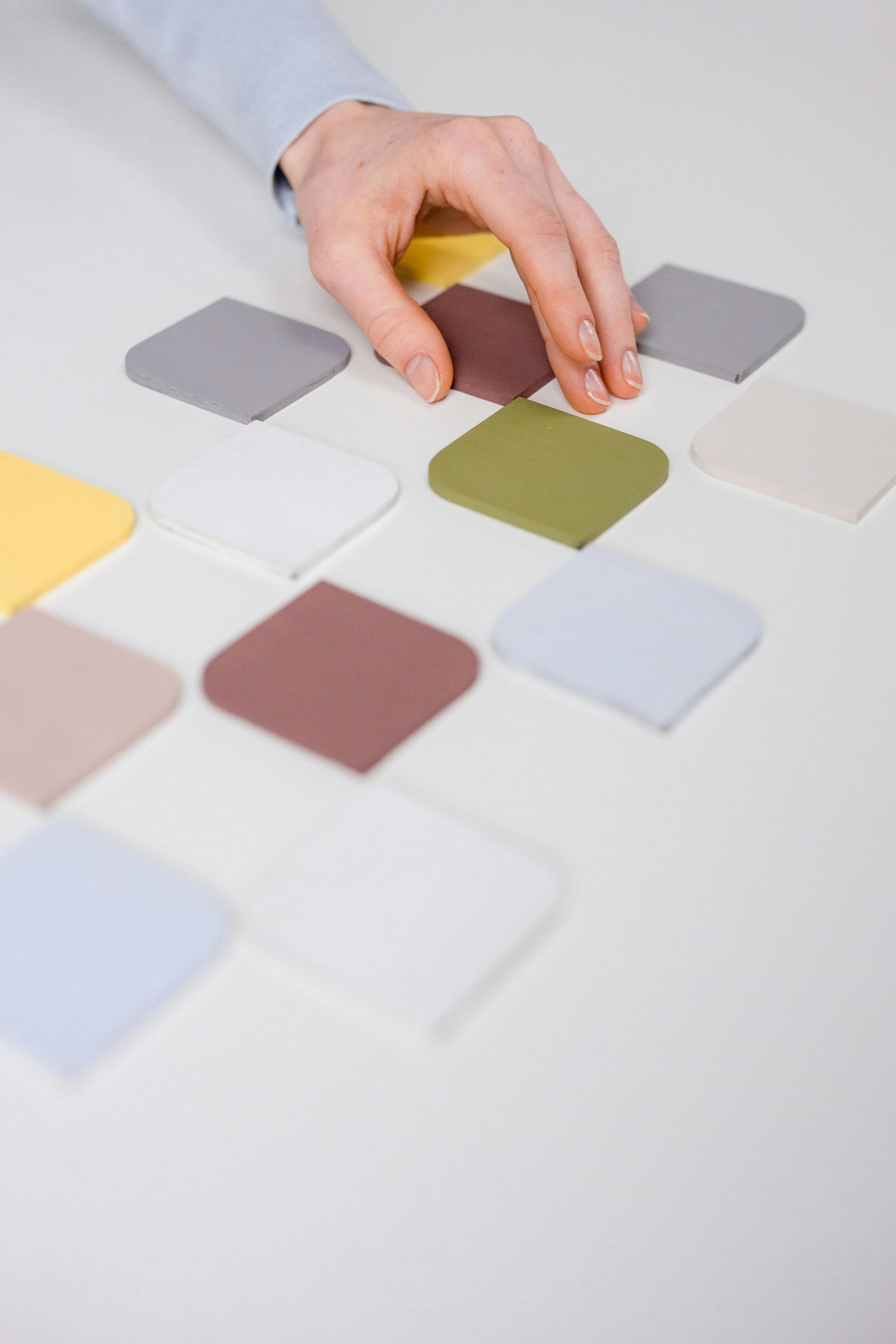 Hand selecting color swatches on a white surface; various pastel hues.