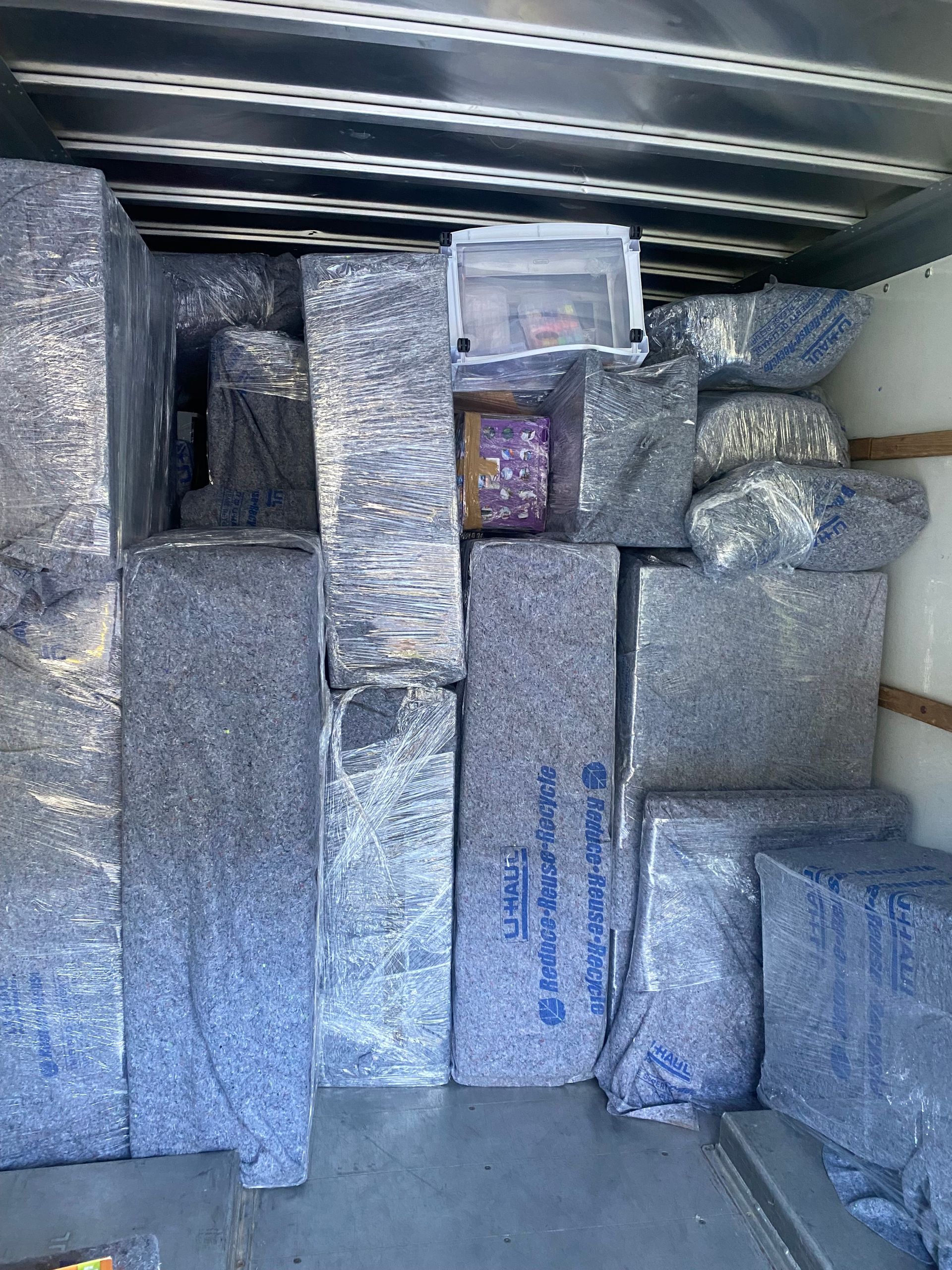 Boxes and furniture wrapped in plastic inside a truck, ready for moving.