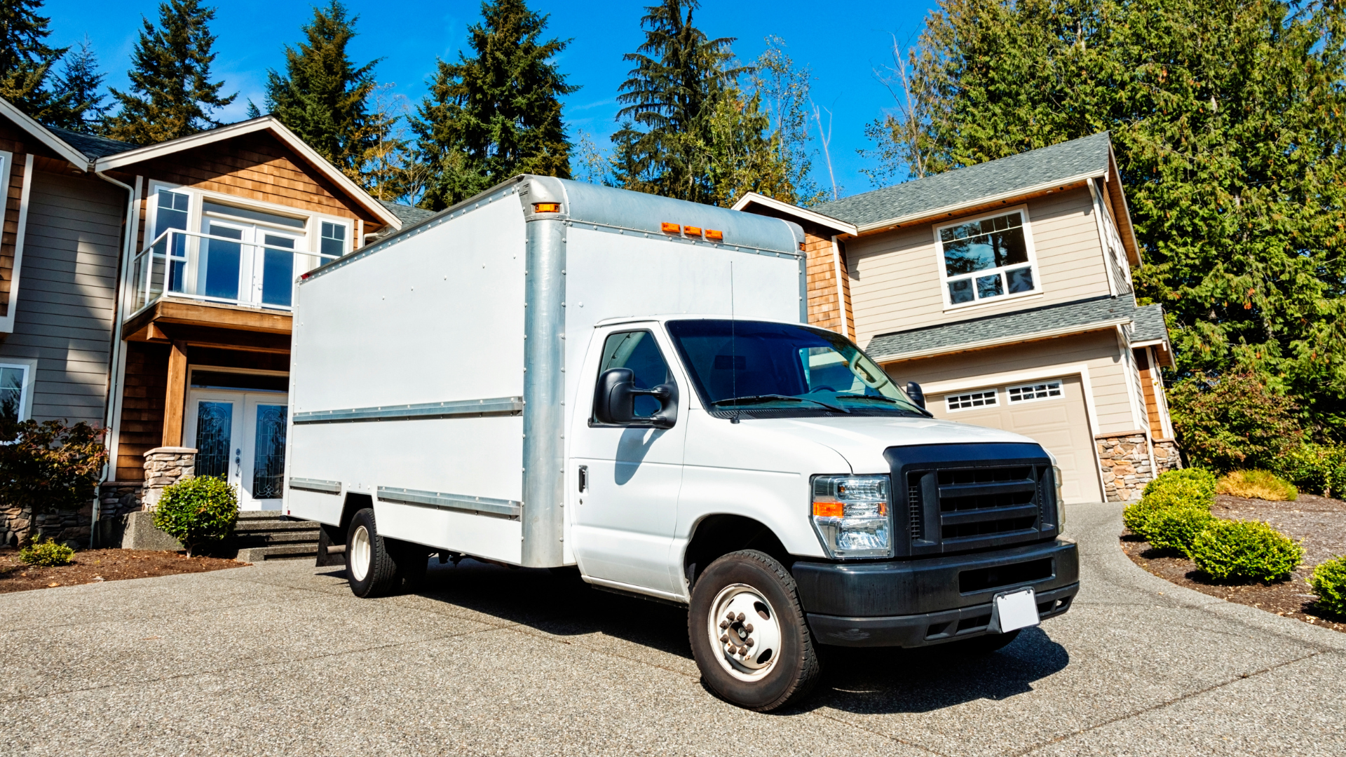 Two delivery workers loading packages into a van. One pulls a cart; the other stands in the van. Outdoors.