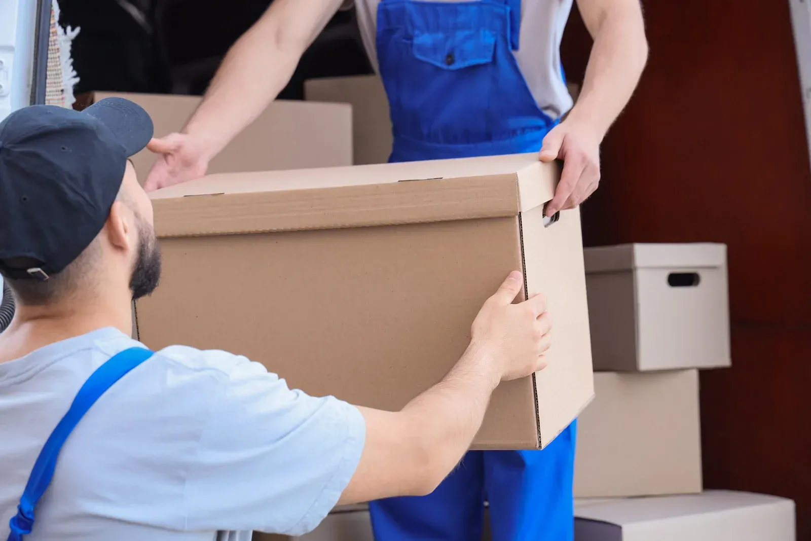 Two delivery workers loading packages into a van. One pulls a cart; the other stands in the van. Outdoors.