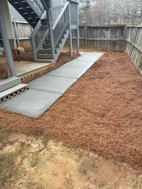 A concrete walkway leading to a deck and stairs in a backyard.