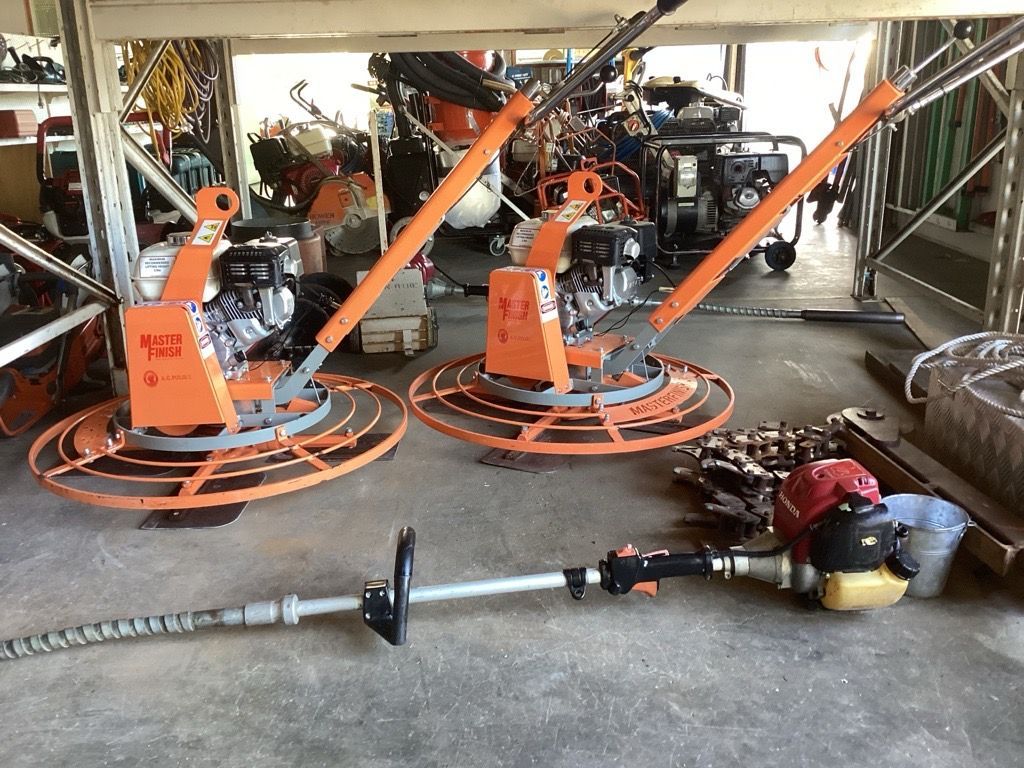 Orange industrial floor scrubbers in a workshop, with a power tool and hose on the floor in front. — Bowen Hire in Bowen, QLD