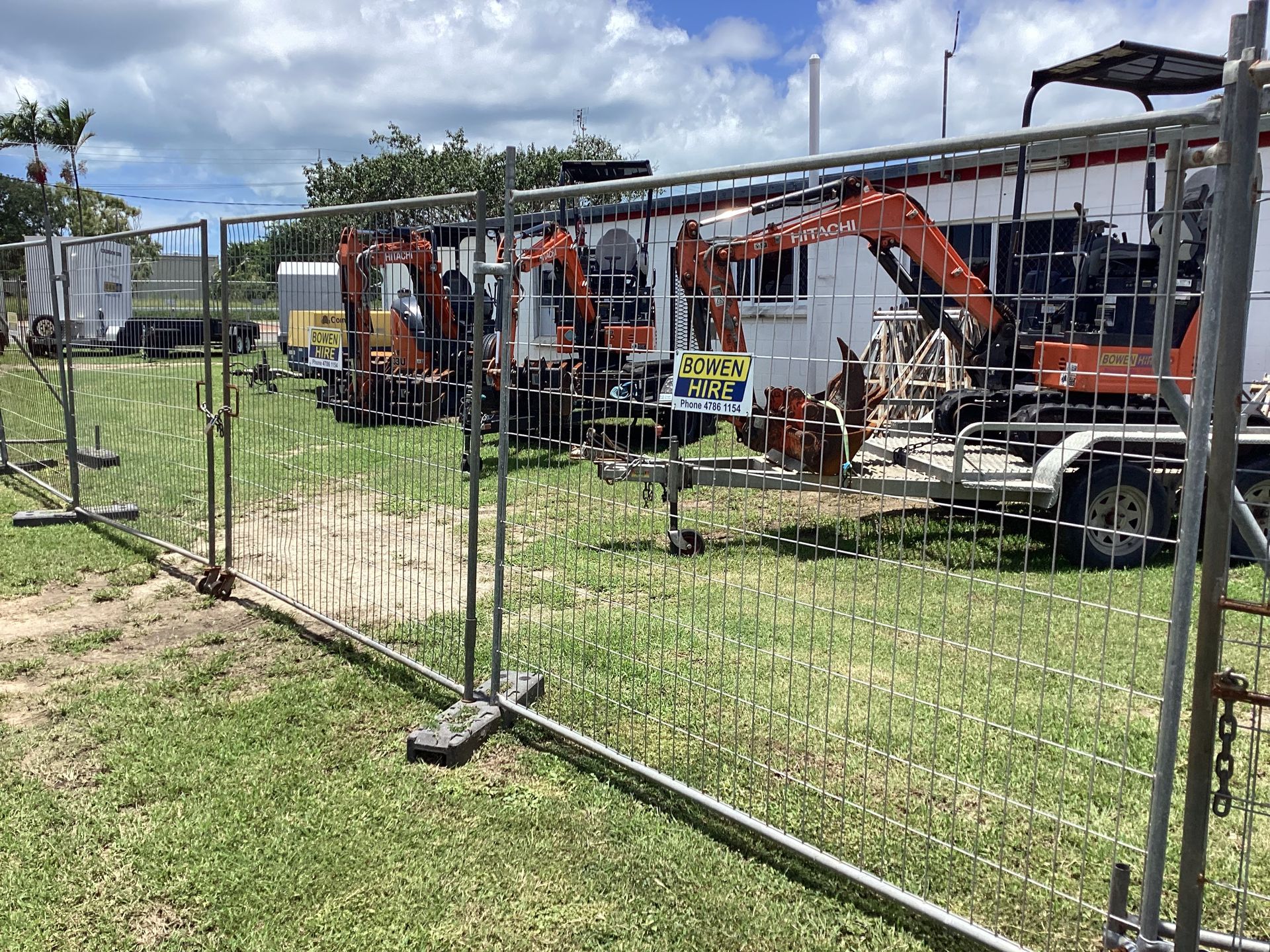 Construction Equipment Parked Behind a Chain-link Fence on a Grassy Lot Under a Blue Sky — Bowen Hire in Bowen, QLD