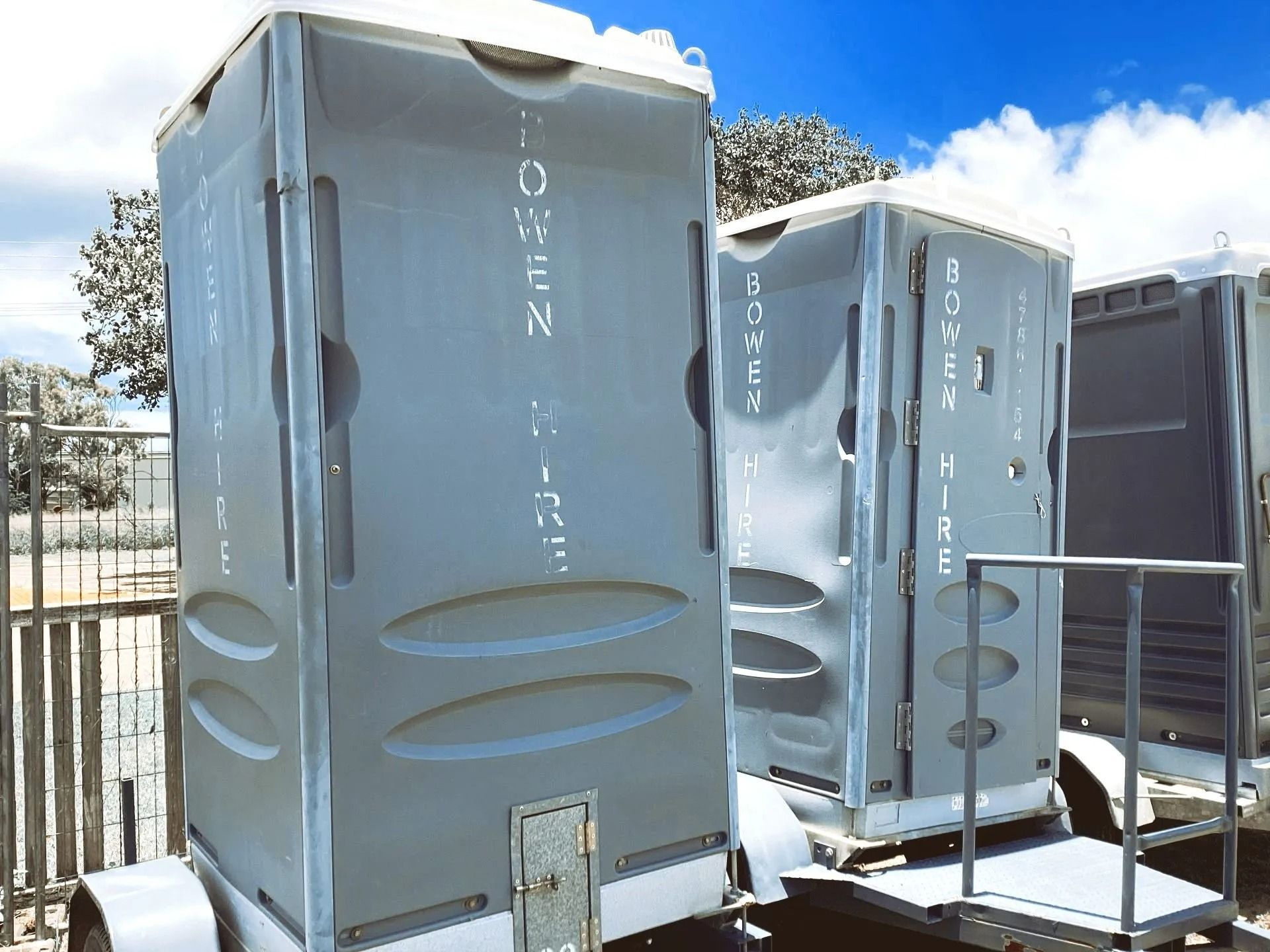 Two Grey Portable Toilets on Trailers Parked Outdoors Under a Blue Sky — Bowen Hire in Proserpine, QLD