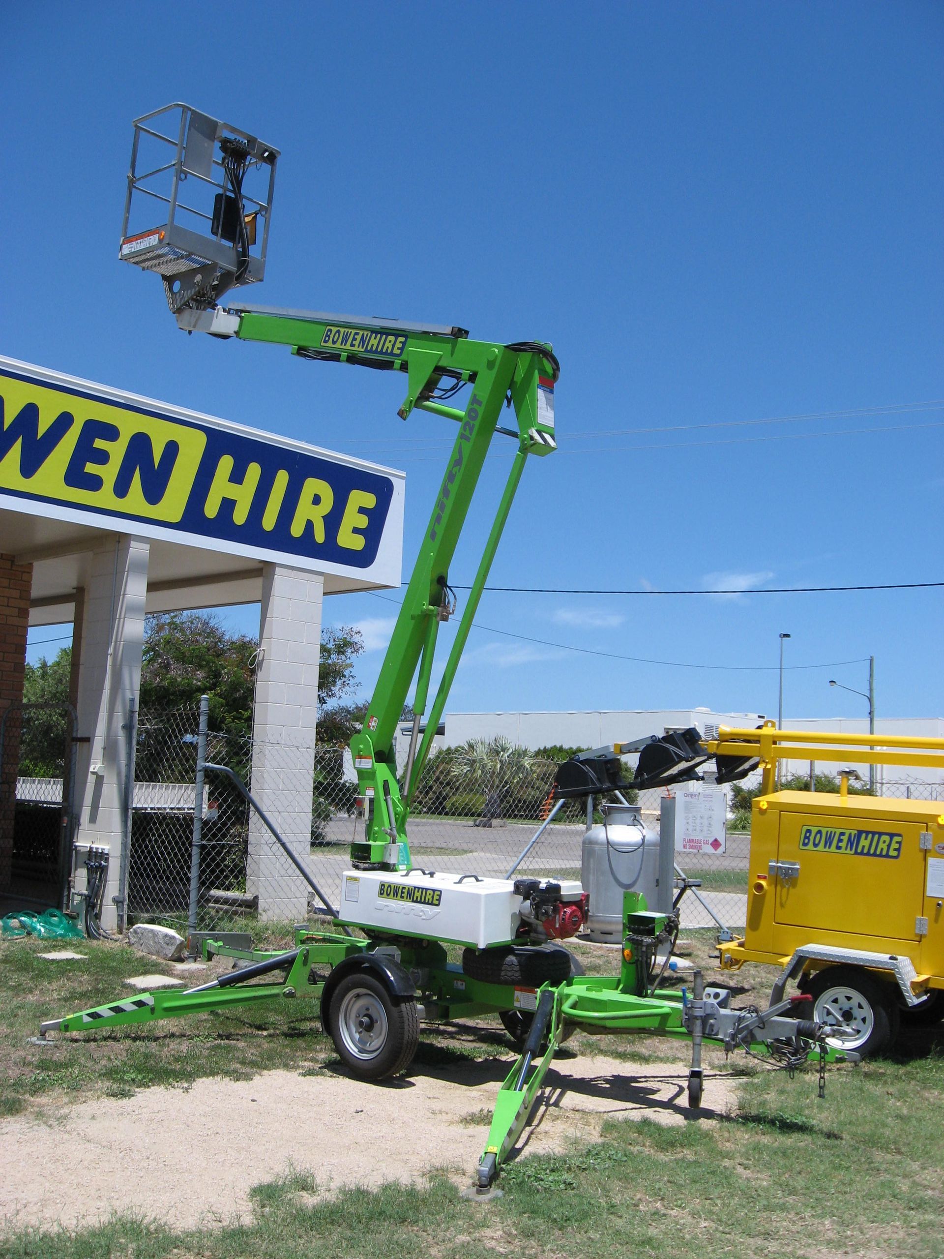 Green Boom Lift Beside a Wem Hire Sign and Yellow Truck Under a Clear Blue Sky — Bowen Hire in Bowen, QLD