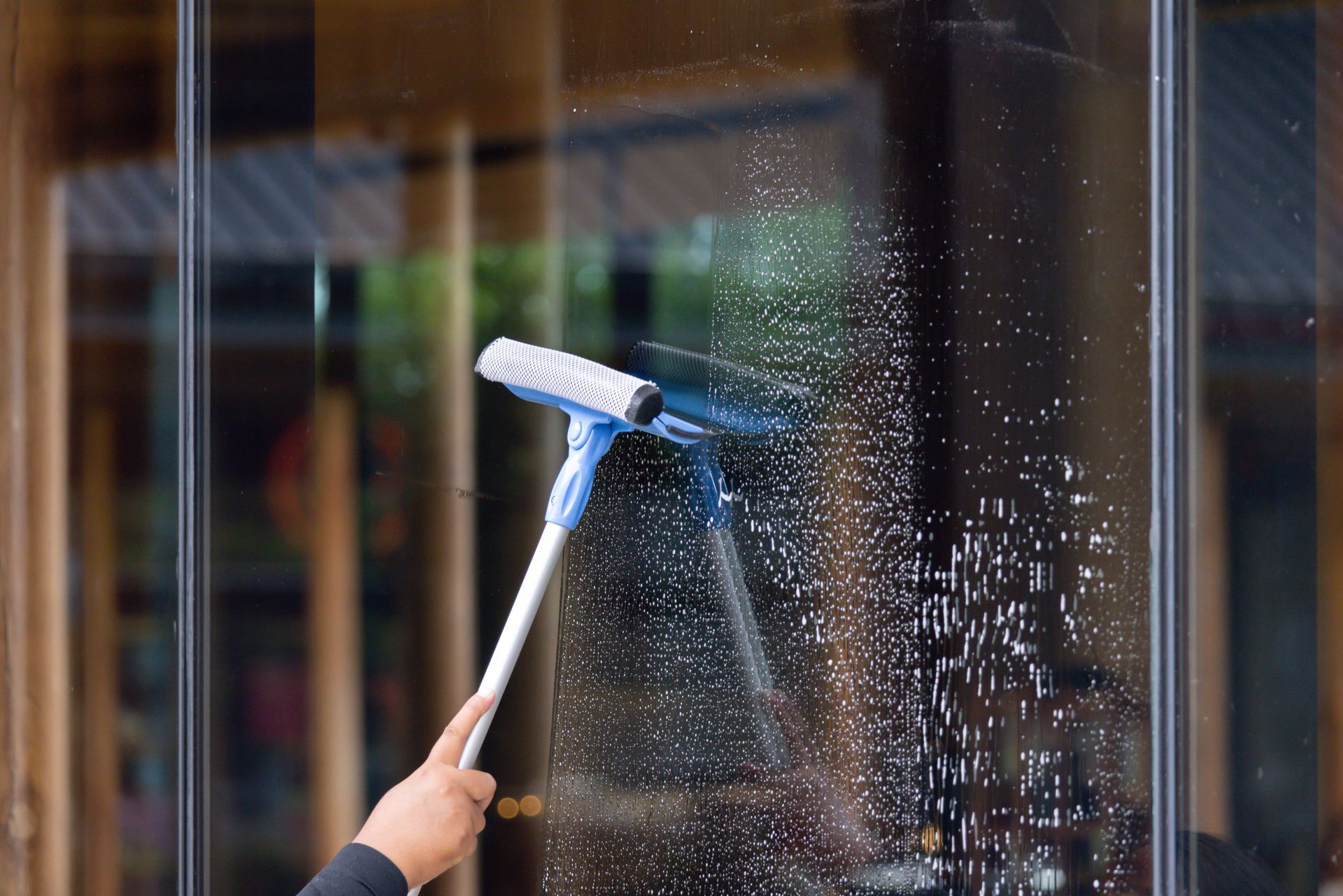 Person cleaning glass window with a blue and white squeegee.