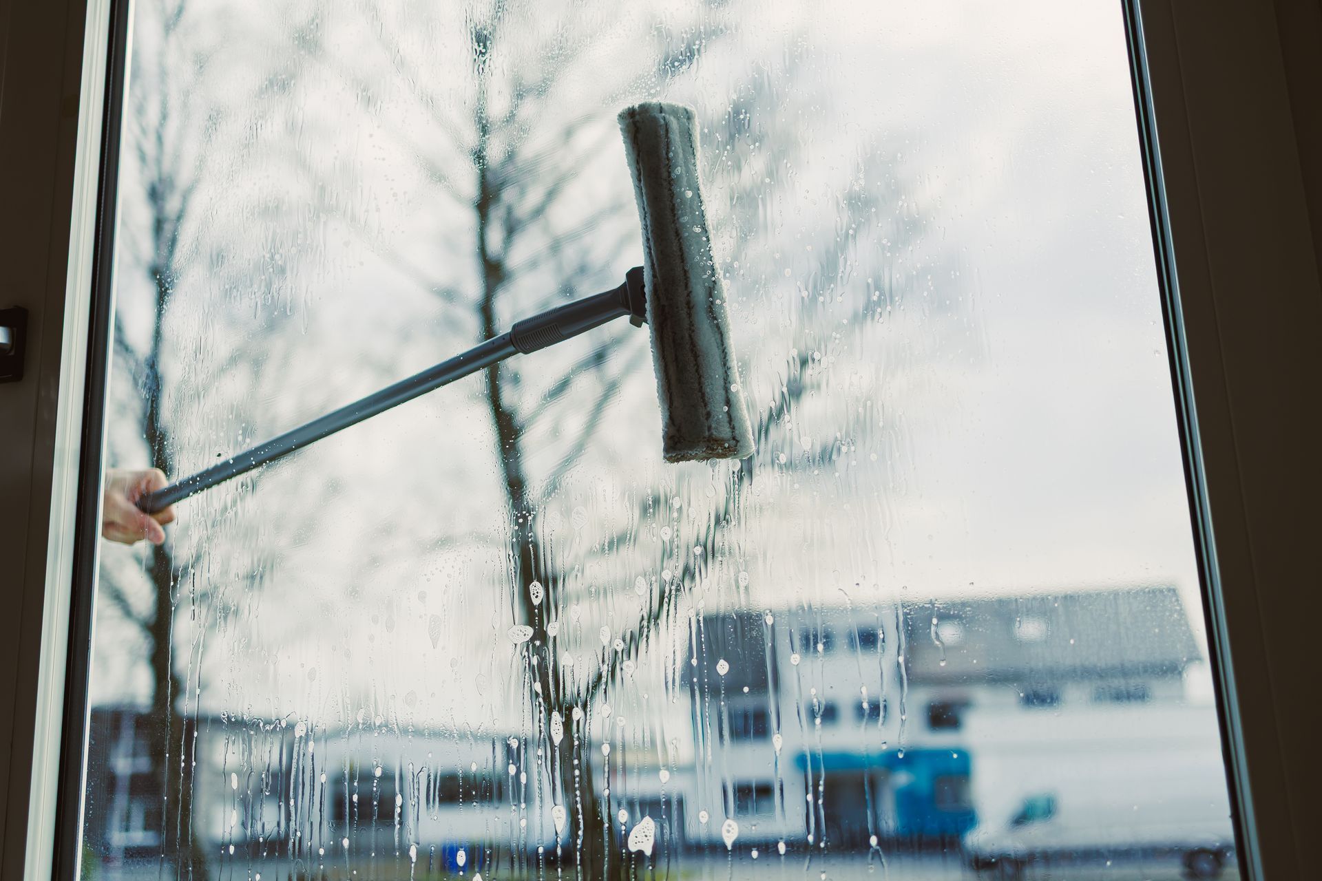 Window being cleaned with a squeegee, blurred outdoor scene visible through the glass.