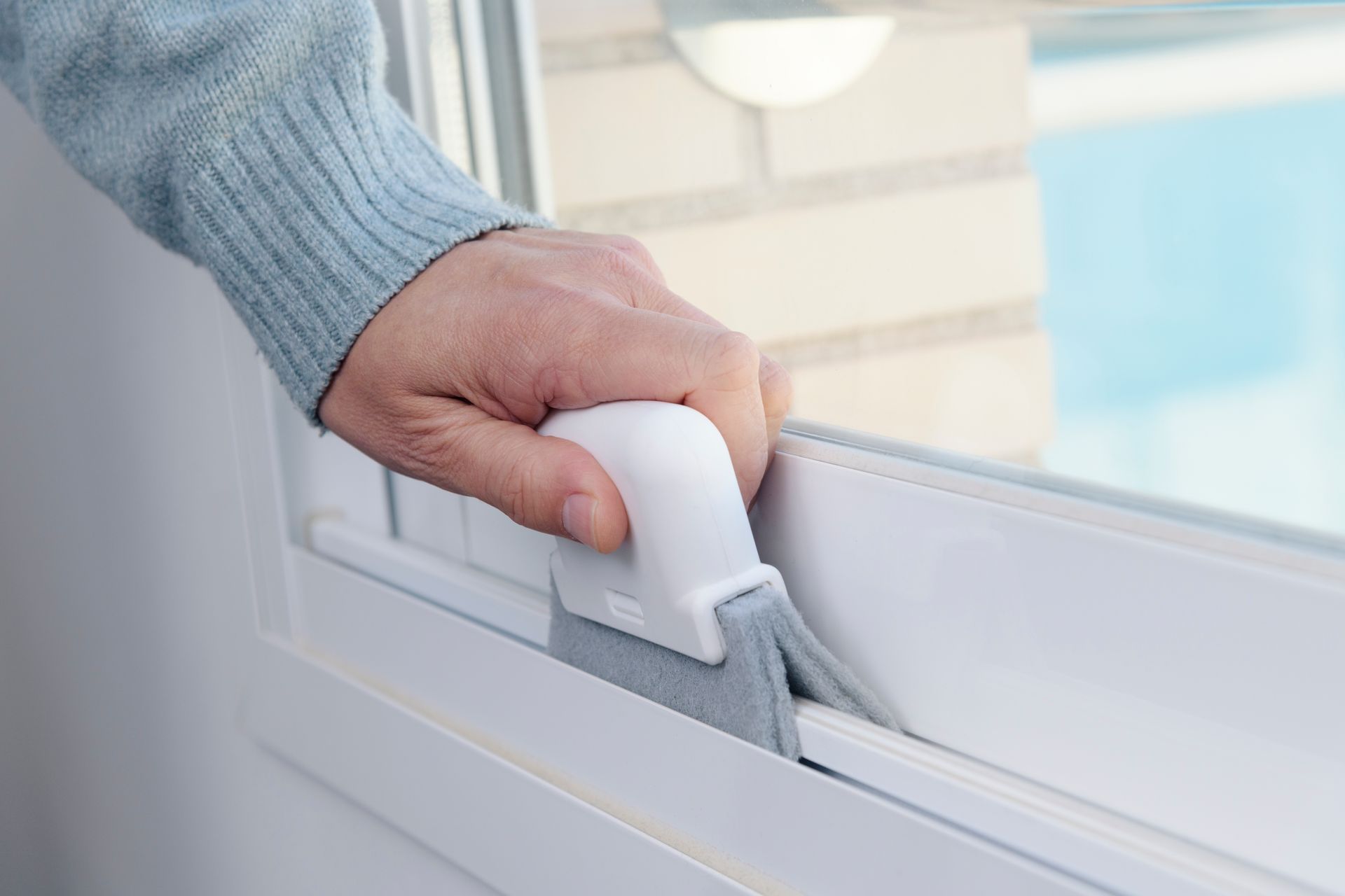 Hand holding a white window cleaning tool, wiping a window in a bright interior.