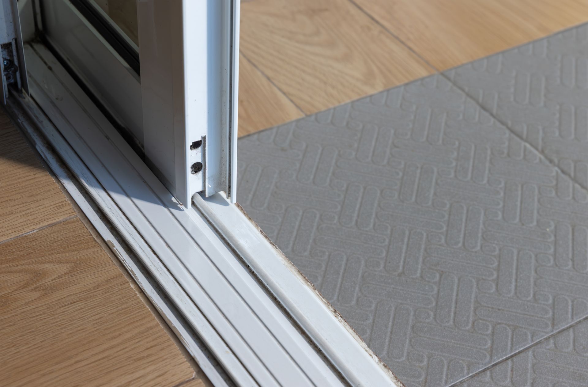A close up of a sliding glass door and tracks against a tiled floor.