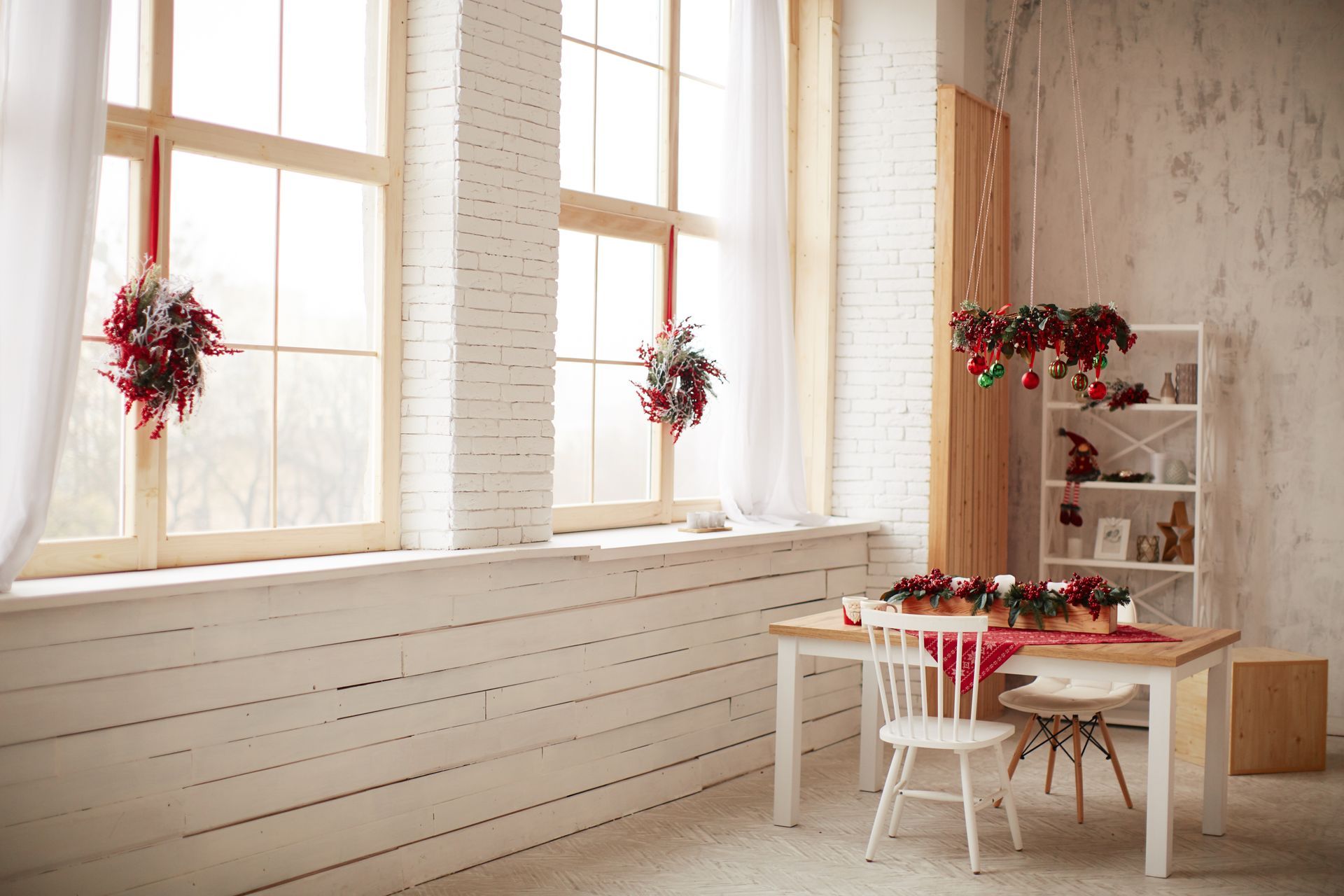 Bright room with windows, decorated for Christmas. Table set with red runner, wreath decor.
