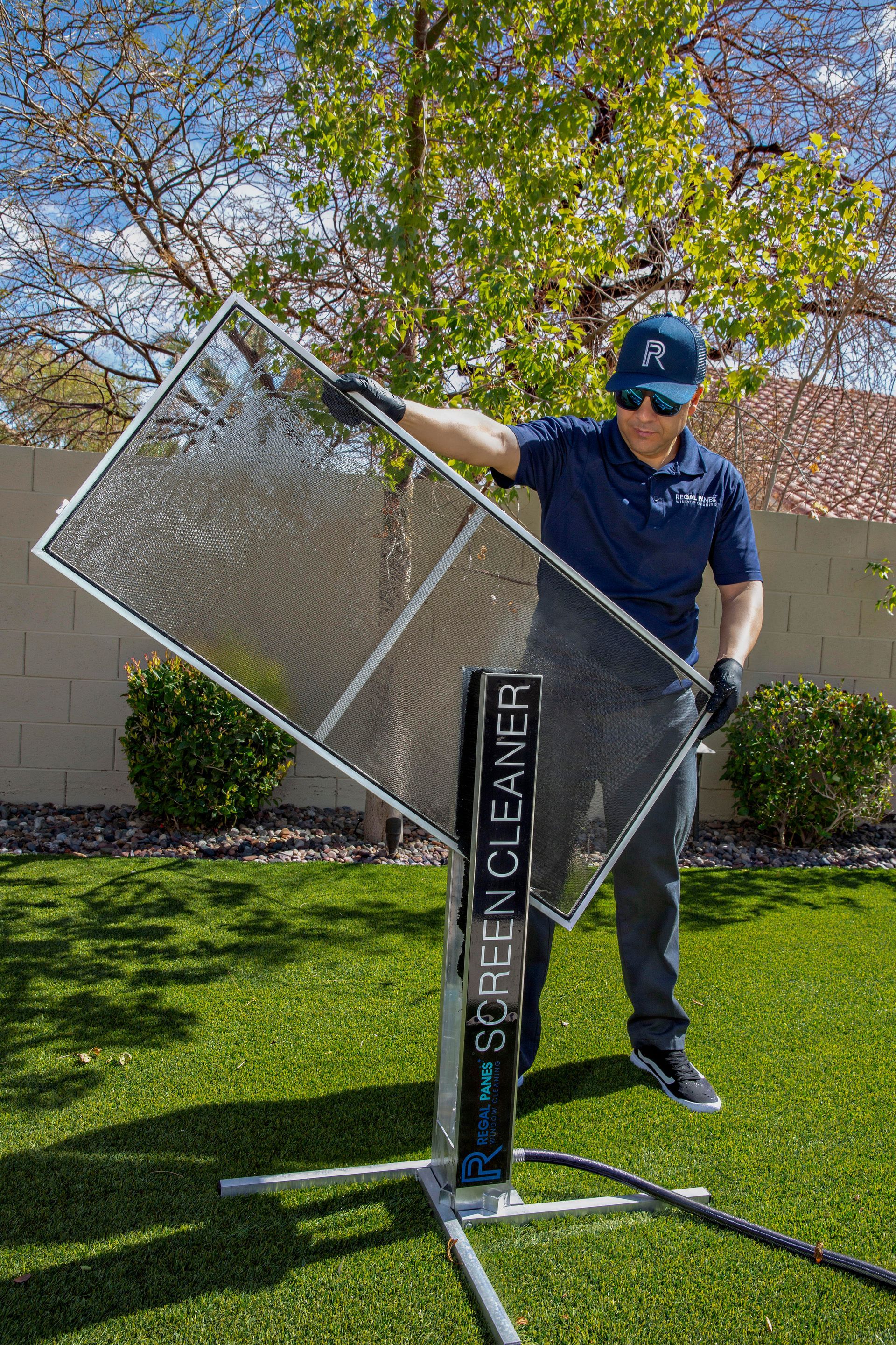 Man washing a screen with water in a backyard using a screen cleaning machine.