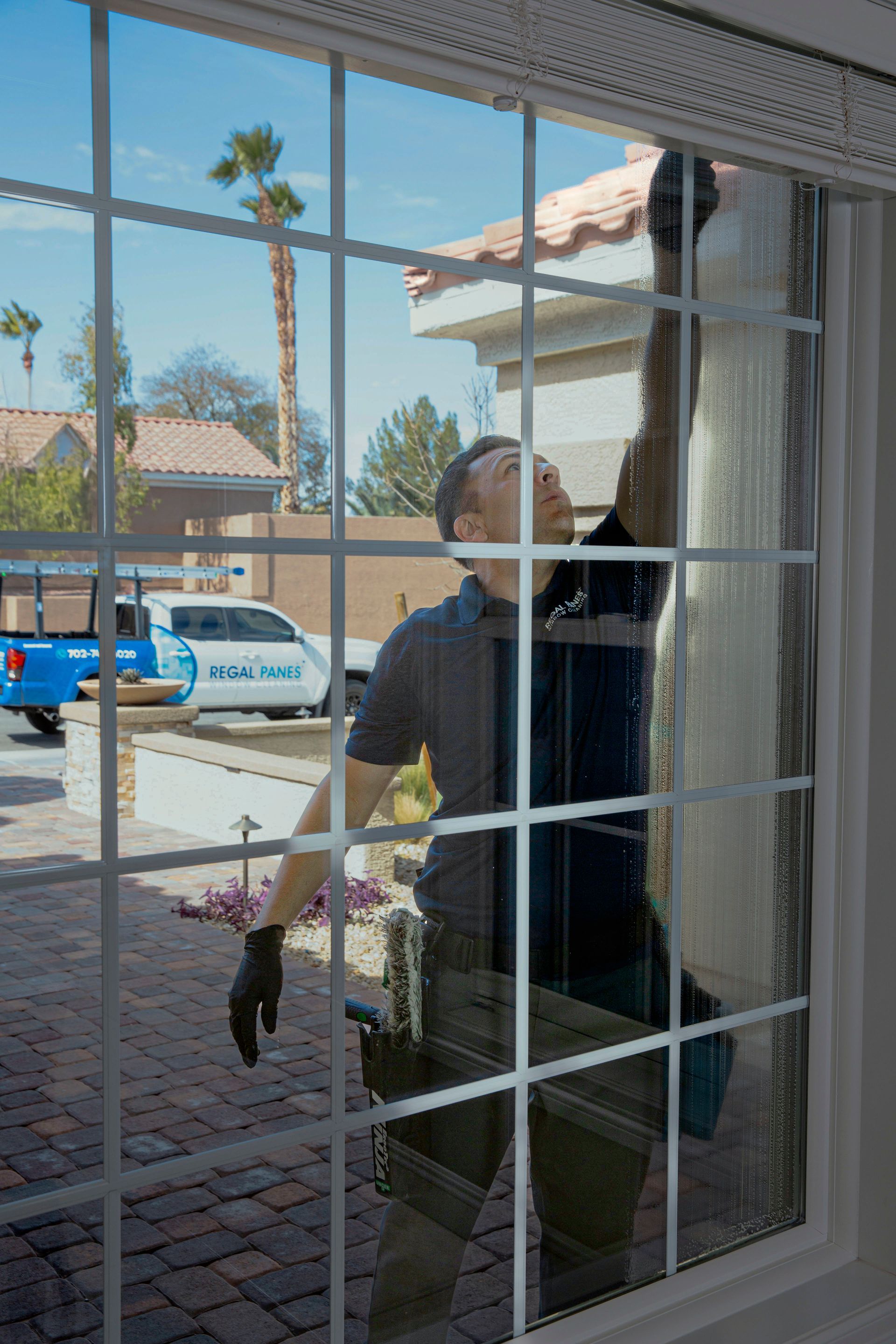 Man washing a window with a squeegee; house and van visible outside.