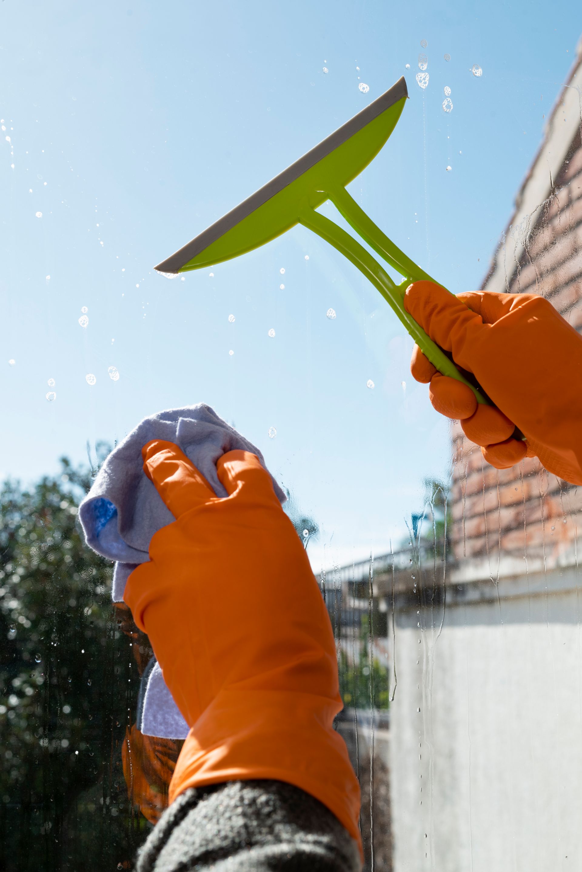 A person wearing orange gloves is cleaning a window with a squeegee.
