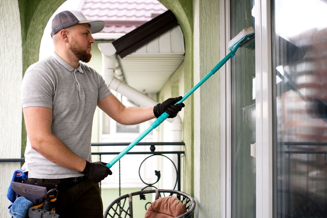 A man is cleaning a window with a broom on a balcony.