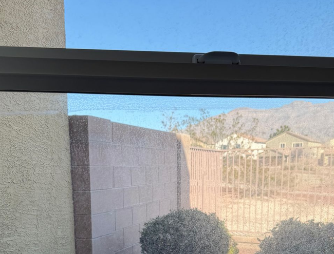 View of a sunlit desert neighborhood and mountains through a window with a screen.