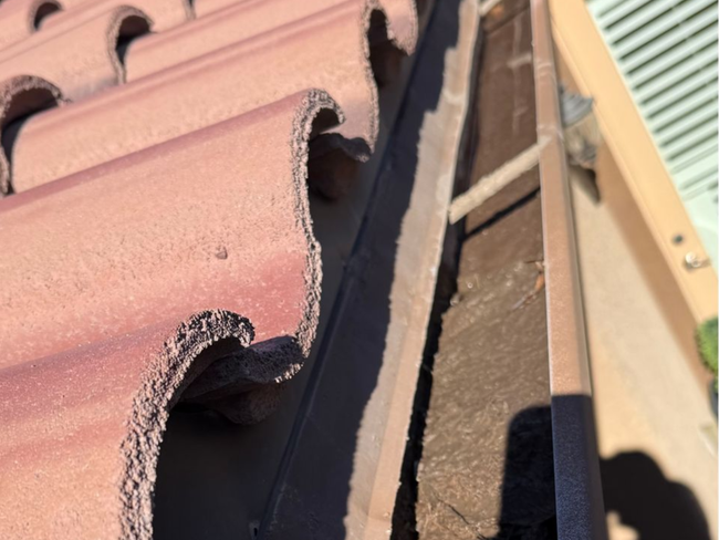A side view of a terracotta tiled roof edge meeting a metal gutter system on a sunny day.