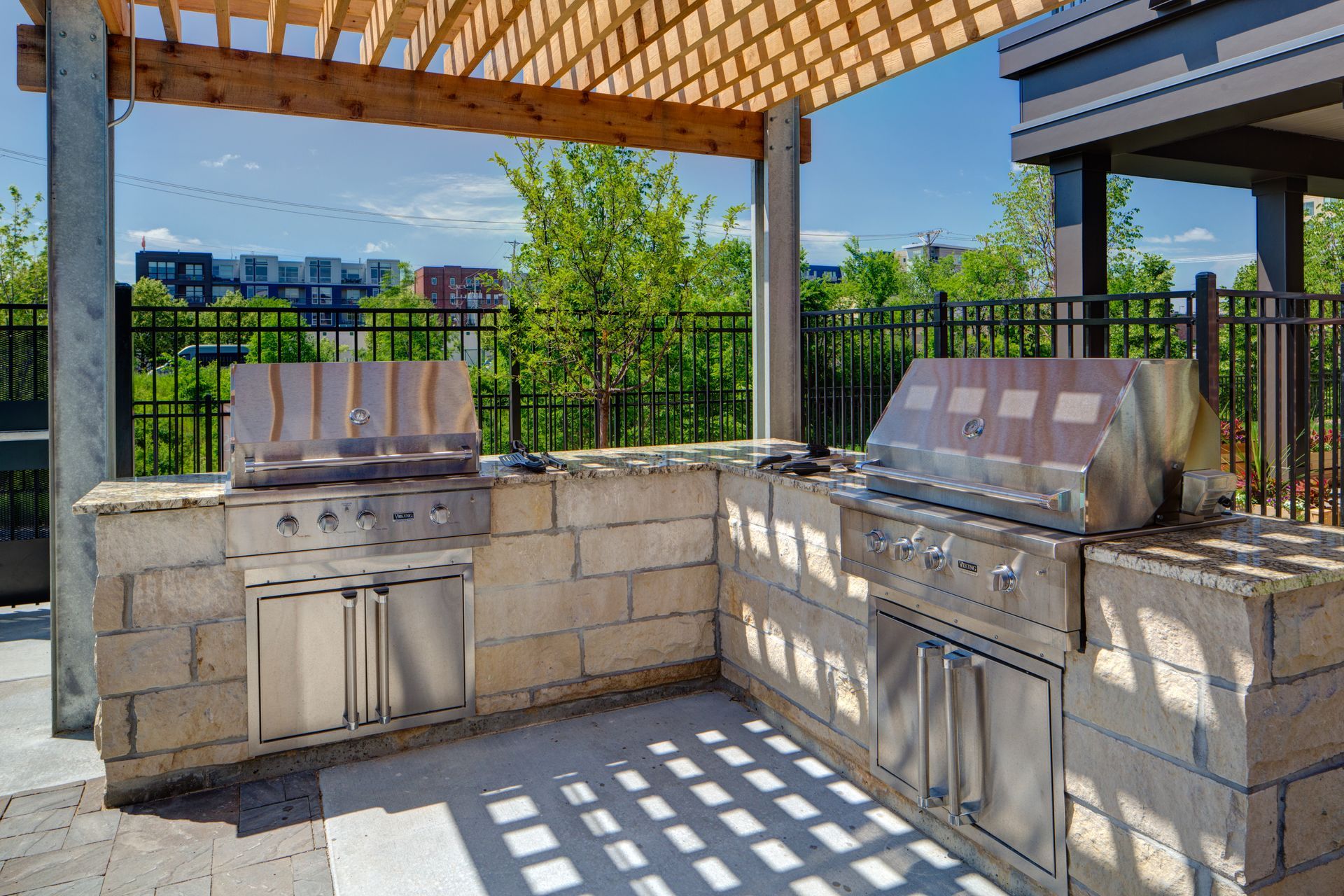 A stainless steel grill is sitting under a wooden pergola.