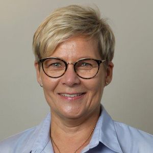 En kvinde med briller og blå skjorte smiler til kameraet.