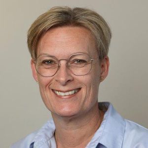En kvinde med briller og blå skjorte smiler til kameraet.