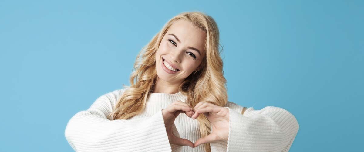 En kvinde i en hvid sweater laver en hjerteform med sine hænder.