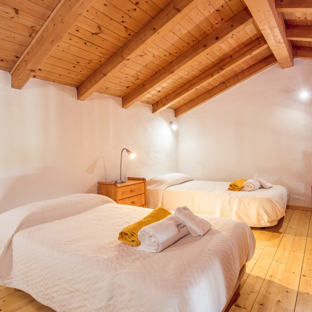 Quarto com duas camas, teto e piso de madeira; toalhas nas camas.