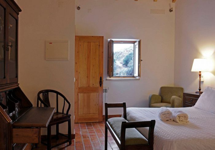 Quarto com cama, escrivaninha, cadeira, janela, porta de madeira e poltrona.