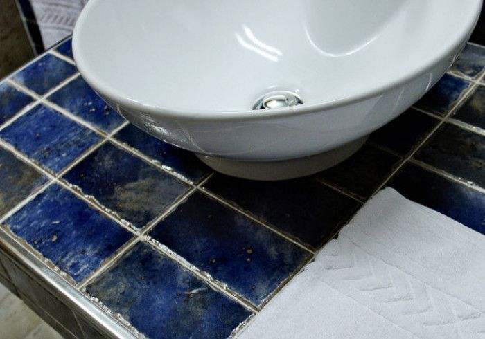 Cuba de cerâmica branca sobre bancada de azulejos azuis e pretos.