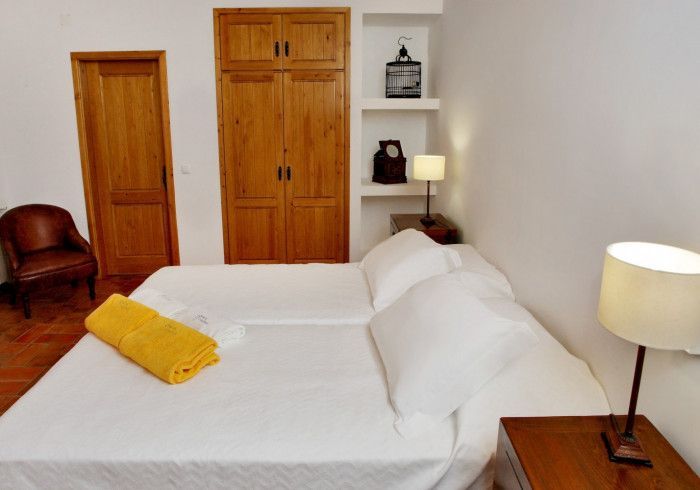 Quarto com duas camas de solteiro, móveis de madeira, roupa de cama branca, toalha amarela e uma pequena área de estar.