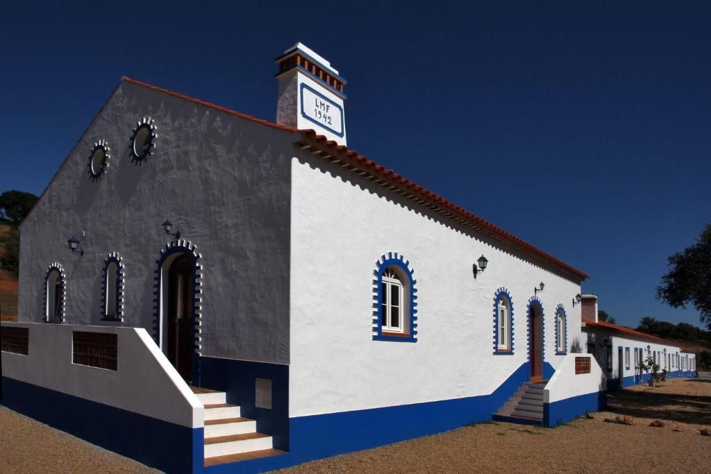 Prédio branco e azul com janelas em arco, telhado de telha vermelha e chaminé contra um céu azul.