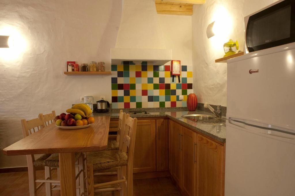 Cozinha com armários de madeira, backsplash de azulejos coloridos e mesa de jantar com frutas.