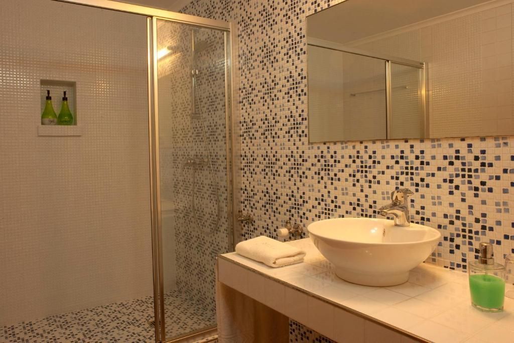 Banheiro moderno com box de vidro, parede revestida com azulejos em mosaico e pia branca sobre bancada branca.