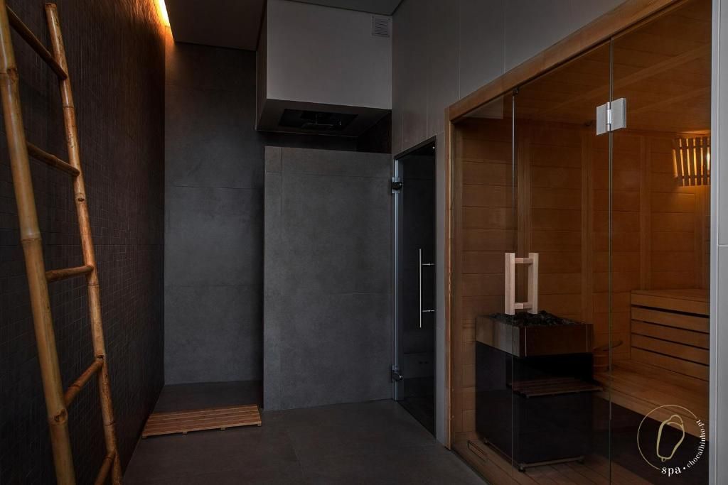 Interior de spa moderno com paredes escuras, sauna de madeira e escada de bambu.