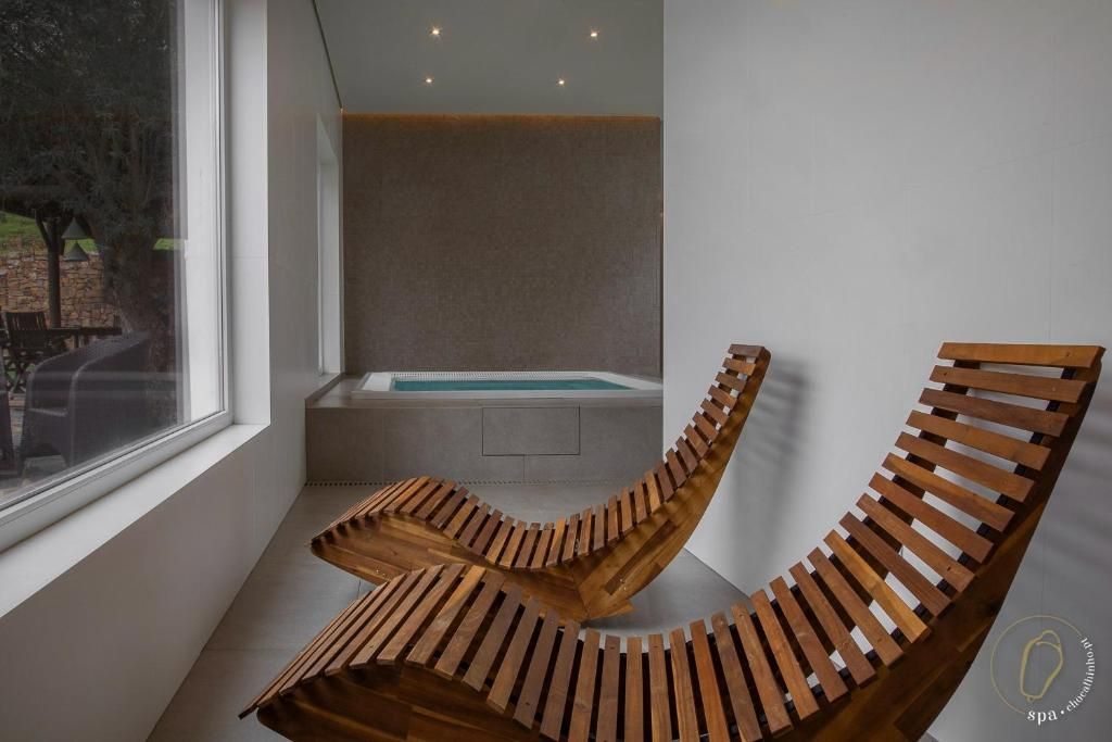 Duas espreguiçadeiras de madeira junto a uma janela numa sala de spa com uma pequena piscina.