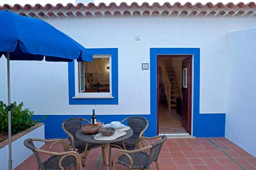 Pátio externo com detalhes em azul, mesa posta para refeições e porta parcialmente aberta.