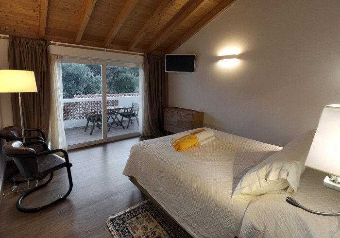 Quarto com cama, varanda e teto de madeira. A mobília inclui uma cadeira, luminárias e um tapete.