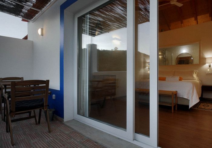 Pátio com mesa, cadeiras e porta de vidro deslizante que dá acesso a um quarto com cama.