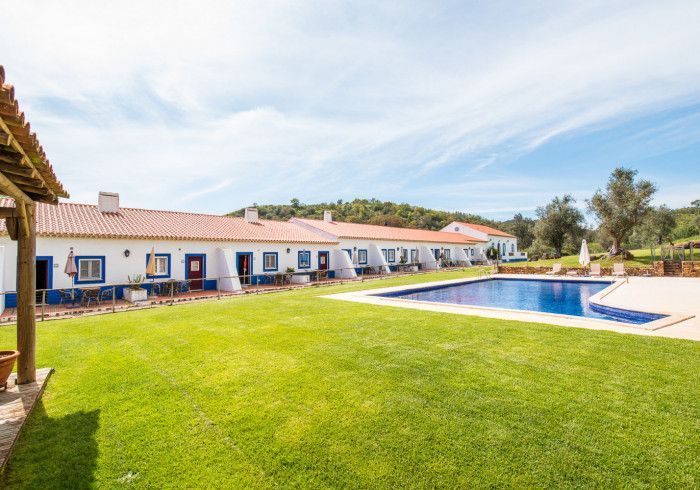 Fileira de prédios brancos com detalhes em azul, telhado de telha vermelha e uma piscina em um gramado.