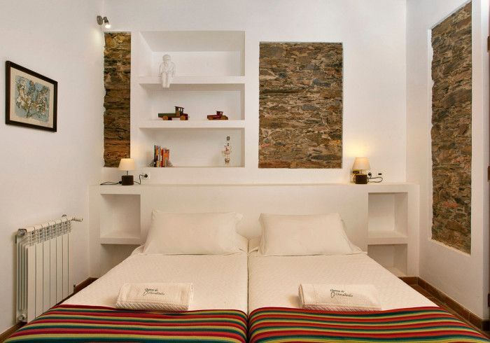 Quarto com duas camas, prateleiras embutidas, detalhes em pedra na parede, luminárias e um radiador na parede.