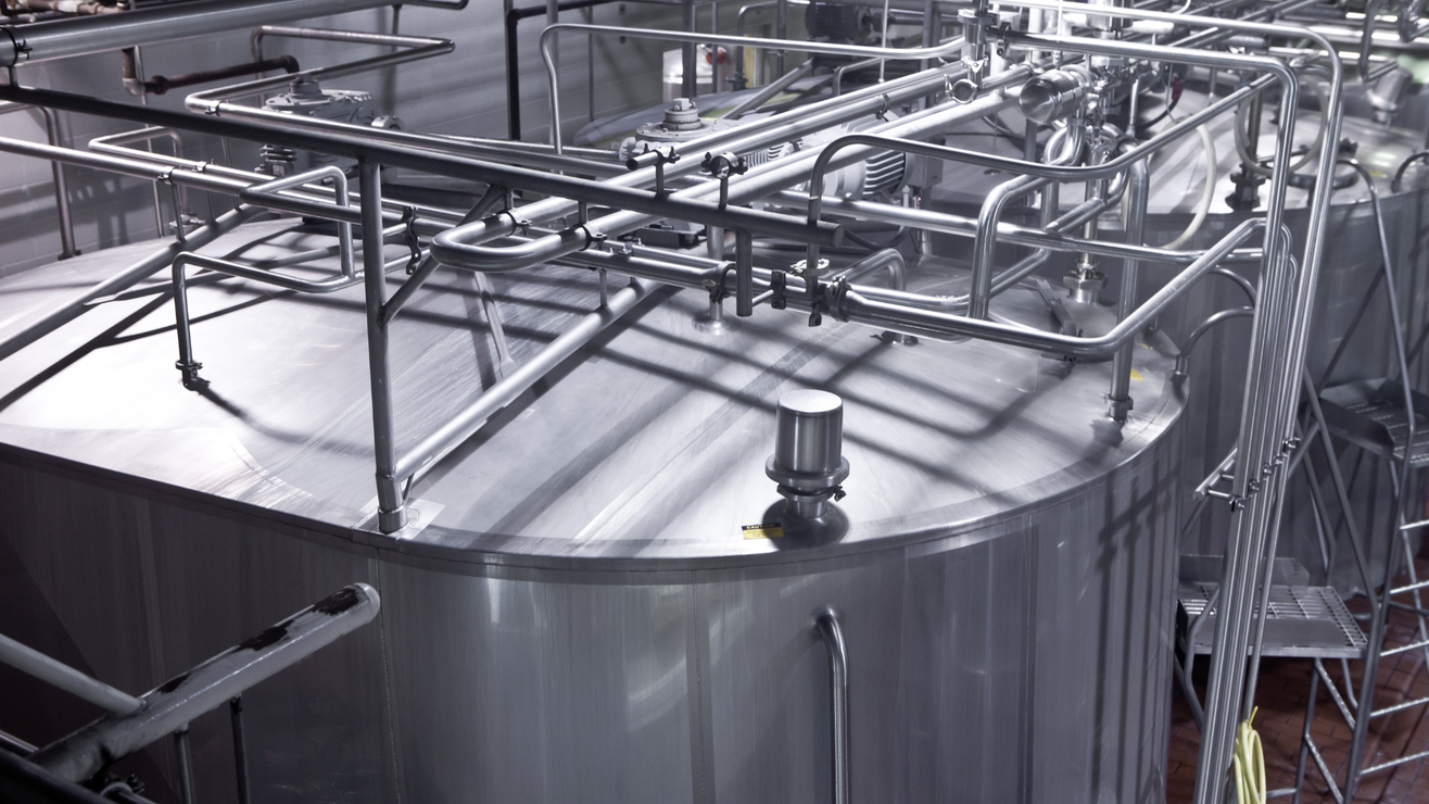 A large stainless steel tank in a factory with pipes coming out of it