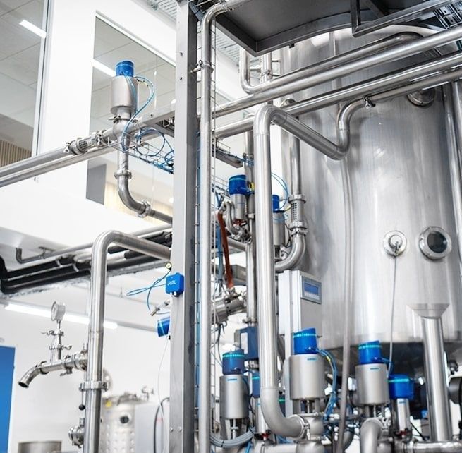 A factory with a lot of stainless steel tanks and pipes.