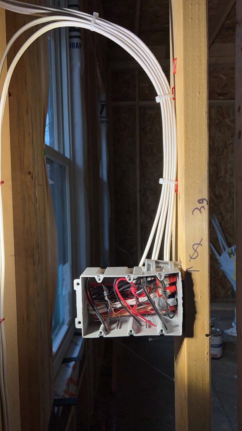 Electrical wiring box installed between wooden wall studs, cables arching above.