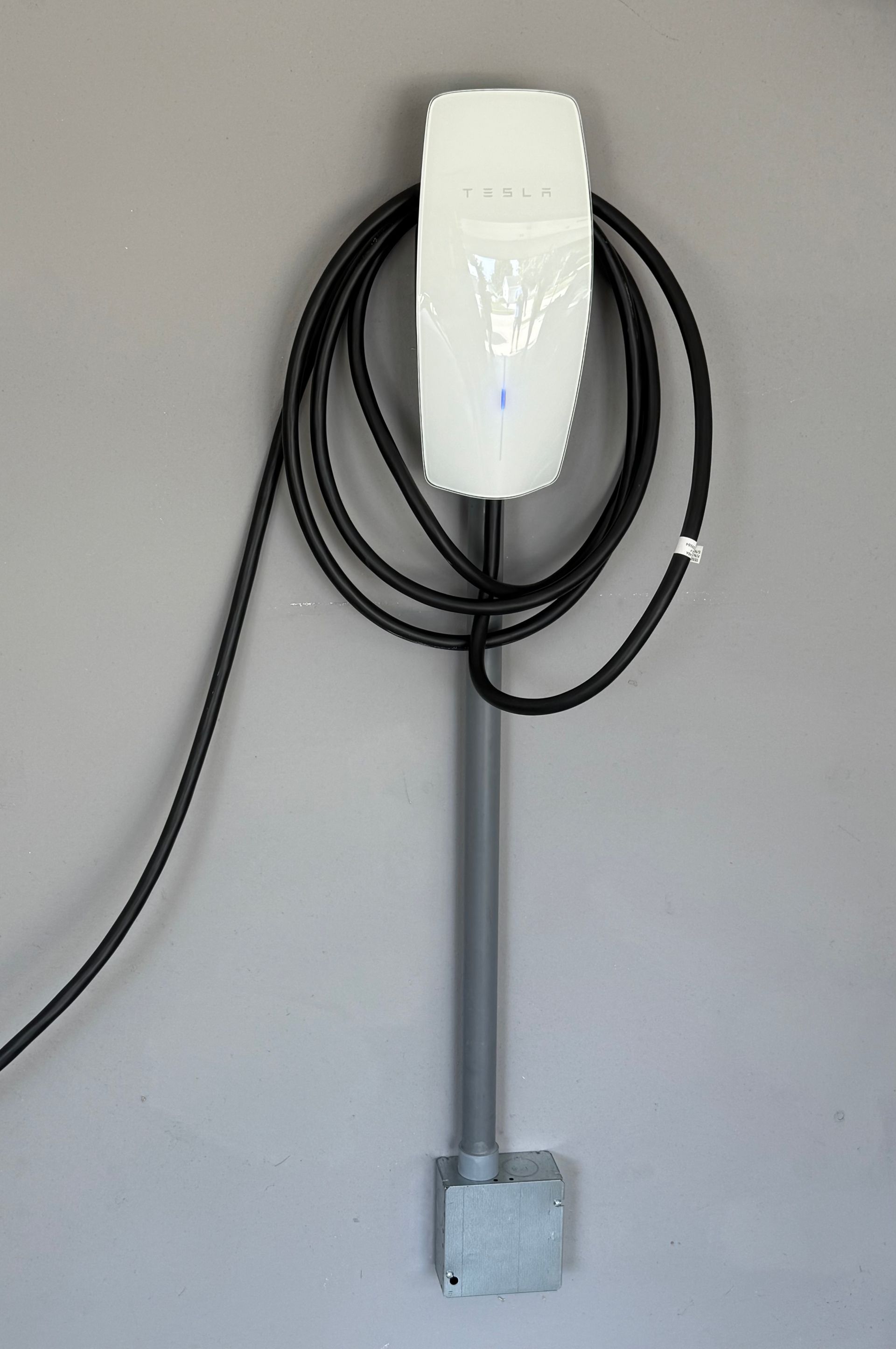 Tesla EV charger mounted on gray wall with coiled black cable.