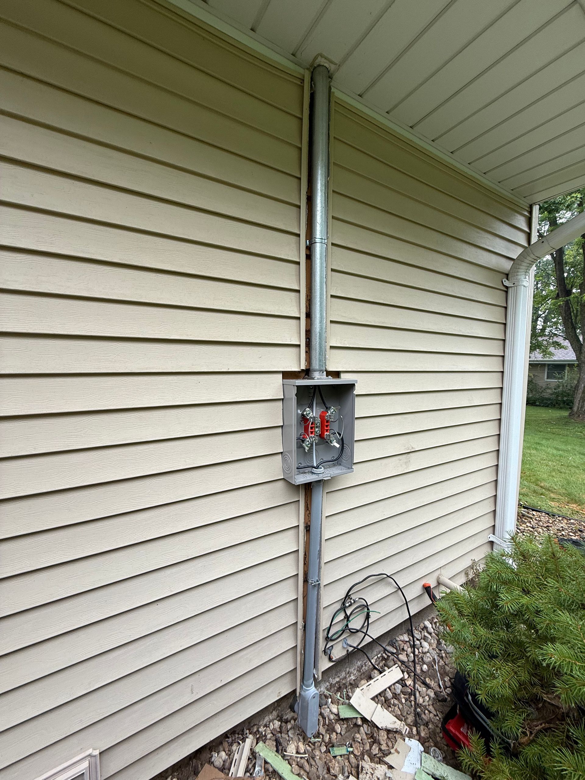 Exterior electrical conduit and junction box on a beige house wall with a green lawn in the background.